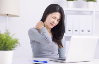 女性在辦公桌前皺眉，用手按住痠痛的肩頸