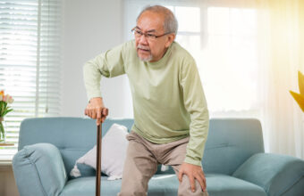 年長男性手扶拐杖，吃力地從沙發上起身