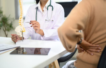醫師手持脊椎模型解說，旁邊的人以手扶住下背腰部