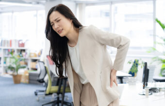 女性在辦公室久坐後用手扶住下背腰部