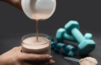 將乳清蛋白飲品倒入玻璃杯，旁邊放著啞鈴