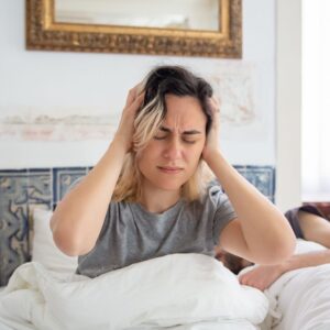 女性早晨坐在床上雙手抱頭，睡醒仍感到疲倦不適