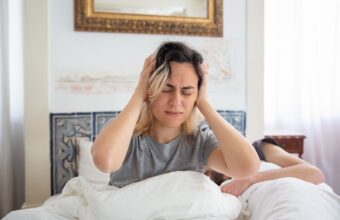 女性早晨坐在床上雙手抱頭，睡醒仍感到疲倦不適